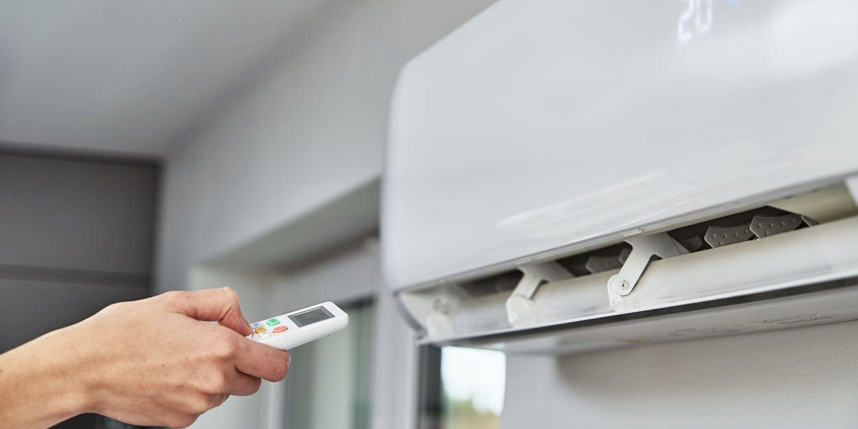 A person holding a remote control on an air conditioner. A person holding a remote control on an air conditioner.