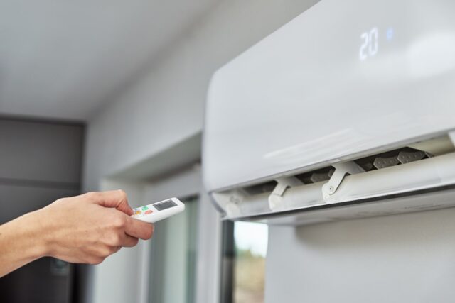 A person holding a remote control on an air conditioner. A person holding a remote control on an air conditioner.
