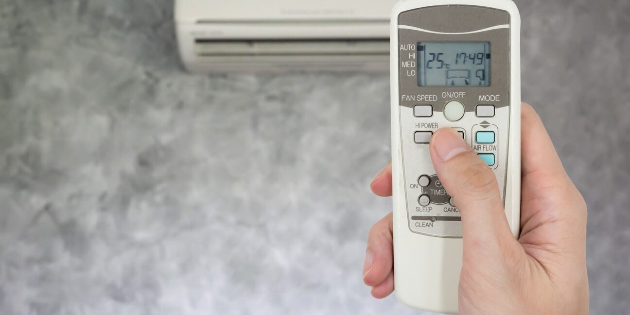 A person holding a remote control in front of an air conditioner.