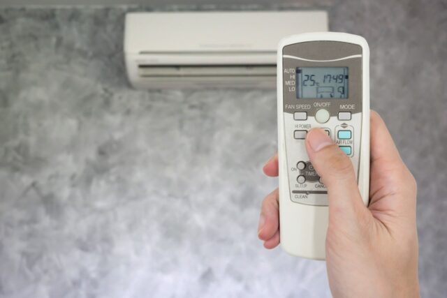 A person holding a remote control in front of an air conditioner. A person holding a remote control in front of an air conditioner.
