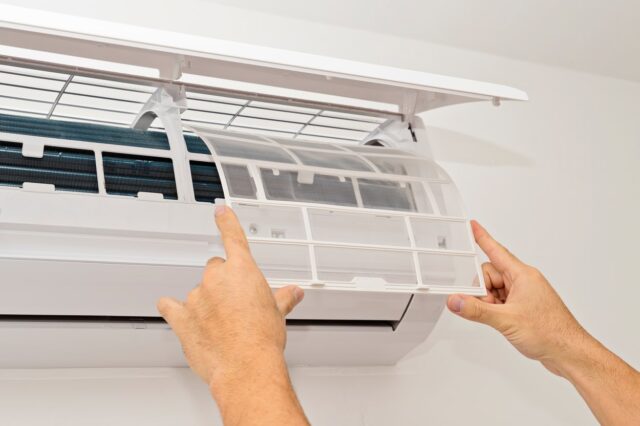 A man is adjusting an air conditioner in a room. A man is adjusting an air conditioner in a room.