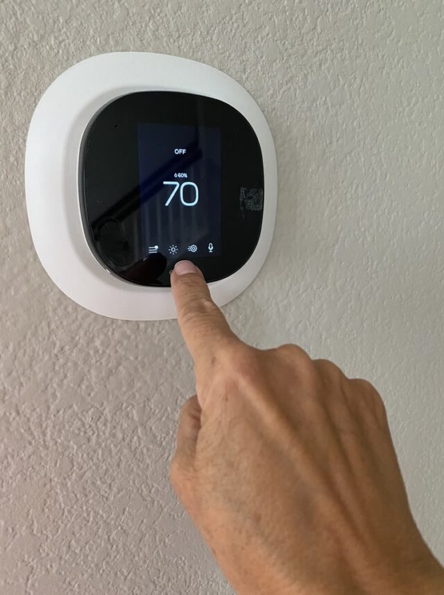 A hand pressing a thermostat. A hand pressing a thermostat.