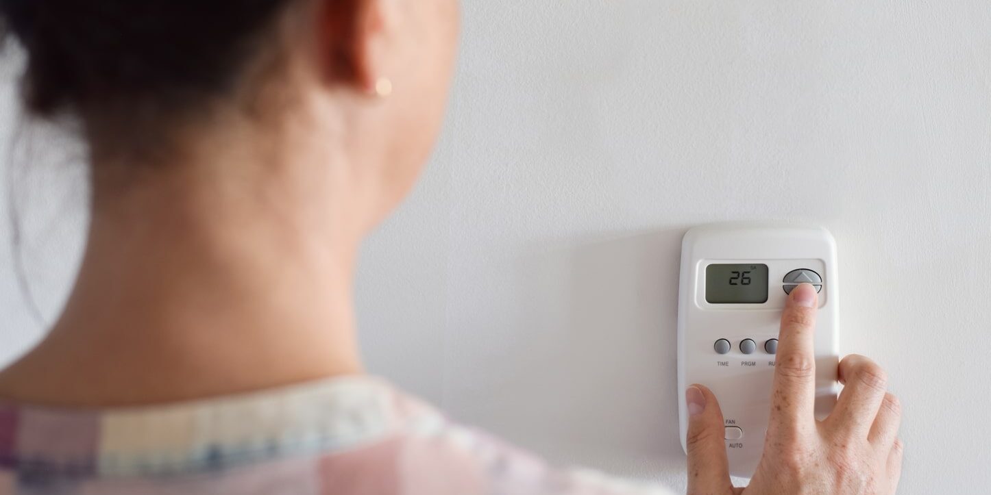 A woman using a digital thermosta on a wall.