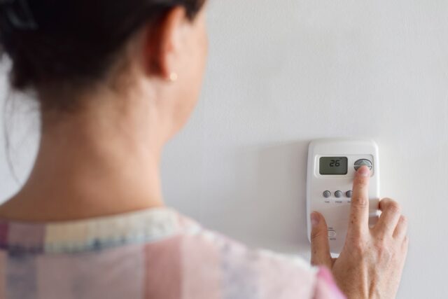 A woman using a digital thermosta on a wall. A woman using a digital thermosta on a wall.