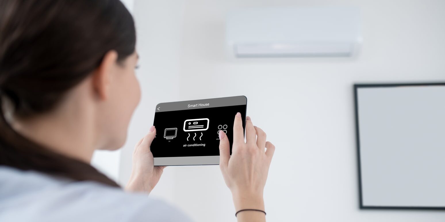 A woman is holding a tablet in front of an air conditioner.