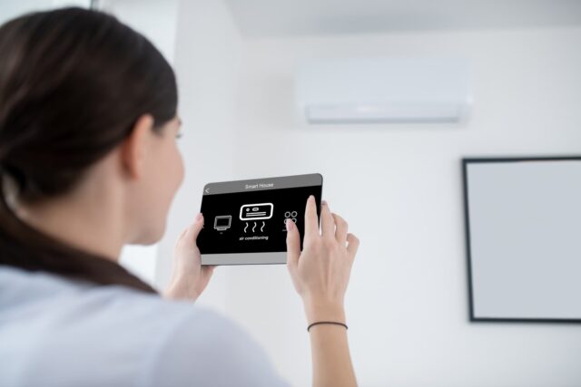 A woman is holding a tablet in front of an air conditioner. A woman is holding a tablet in front of an air conditioner.