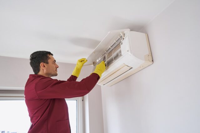 A man cleaning an air conditioner in a room. A man cleaning an air conditioner in a room.
