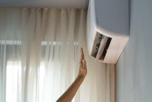 A woman reaching up to a window air conditioner. A woman reaching up to a window air conditioner.