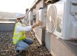 Technician in safety gear inspecting an hvac unit on a rooftop.
