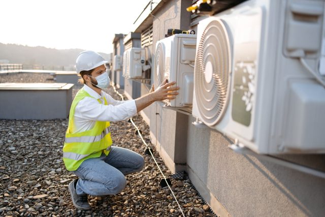 Technician in safety gear inspecting an hvac unit on a rooftop. Technician in safety gear inspecting an hvac unit on a rooftop.