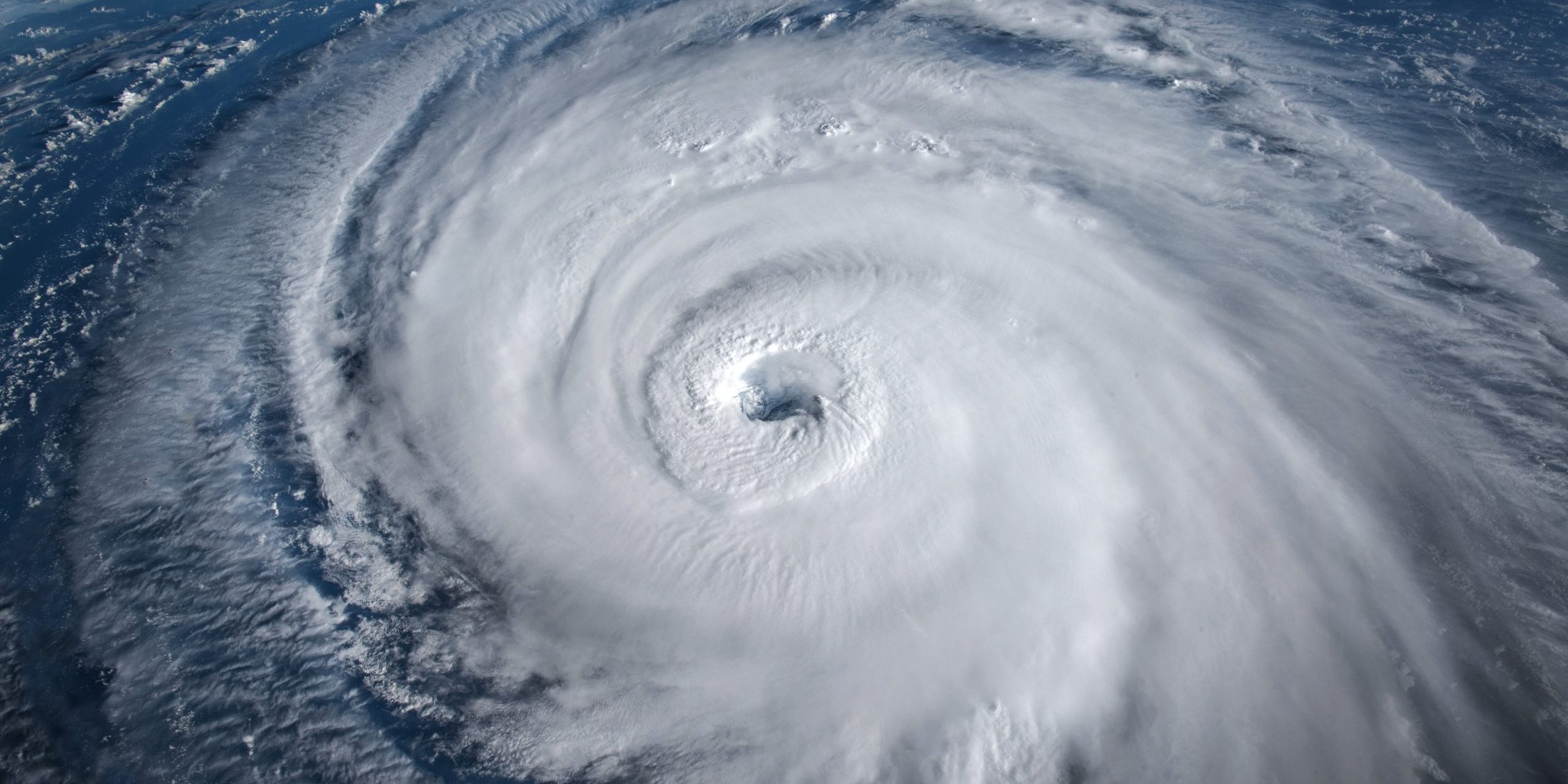 Aerial view of a large hurricane with well-defined eye, swirling clouds and vast spiral bands over the ocean.