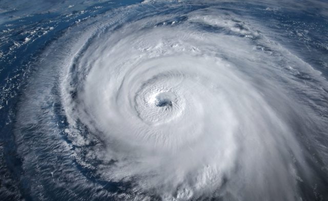 Aerial view of a large hurricane with well-defined eye, swirling clouds and vast spiral bands over the ocean. Aerial view of a large hurricane with well-defined eye, swirling clouds and vast spiral bands over the ocean.