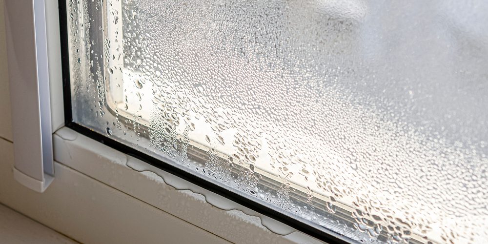 Close-up of a window with condensation on the glass and water droplets collecting at the base of the frame, indicating moisture buildup.