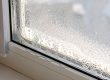 Close-up of a window with condensation on the glass and water droplets collecting at the base of the frame, indicating moisture buildup.
