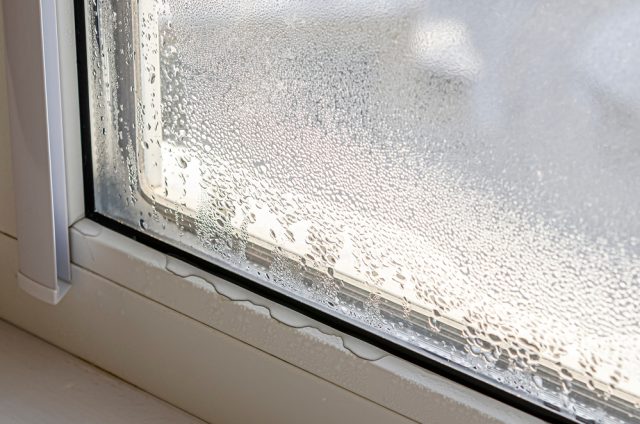 Close-up of a window with condensation on the glass and water droplets collecting at the base of the frame, indicating moisture buildup. Close-up of a window with condensation on the glass and water droplets collecting at the base of the frame, indicating moisture buildup.
