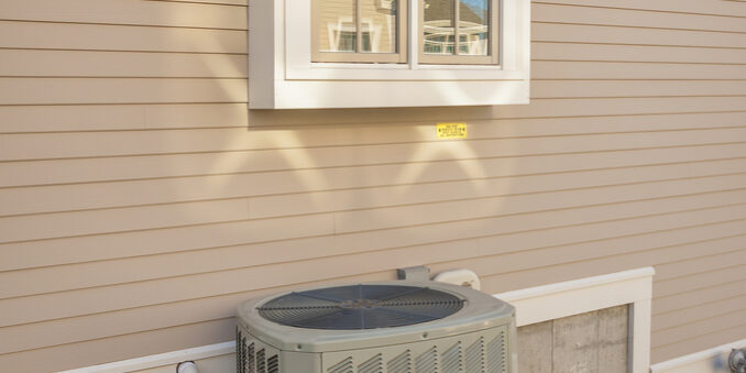An outdoor air conditioning unit sits on a concrete pad next to the beige siding of a house, below a double-hung window. Energy Efficient AC Systems