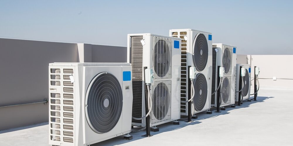 Five large outdoor air conditioning units are installed in a row on a flat rooftop under a clear blue sky. AC systems on roof Commercial Air Conditioning venice Fl