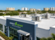 A modern commercial building labeled "ENERGY SMART Sarasota Solutions" with rooftop HVAC units, surrounded by palm trees and distant residential buildings. A professional view of energy-efficient commercial hvac sarasota rooftop units on a modern business building