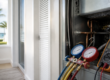 HVAC gauges and a multimeter are attached to an open air conditioning unit inside a modern room with a view of palm trees outside in a service provided by Brisk Air Conditioning for AC Repair Venice FL